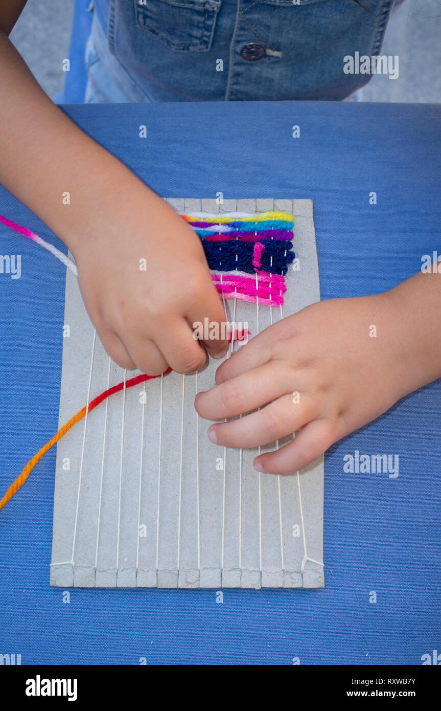 Child girl learning to use cardboard weaving loom. Manual arts