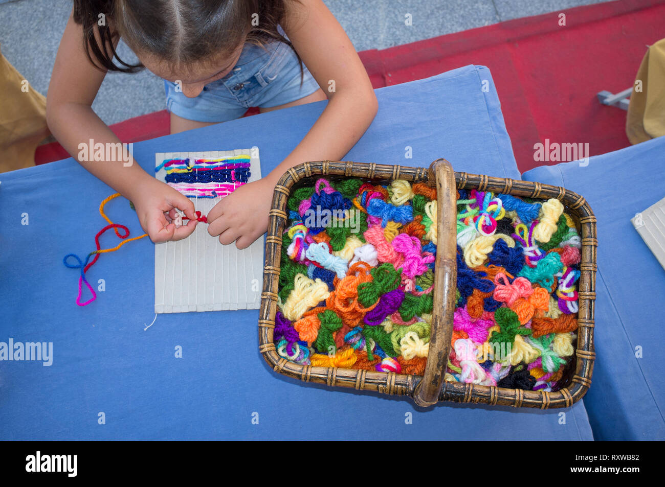 Child girl learning to use cardboard weaving loom. Manual arts