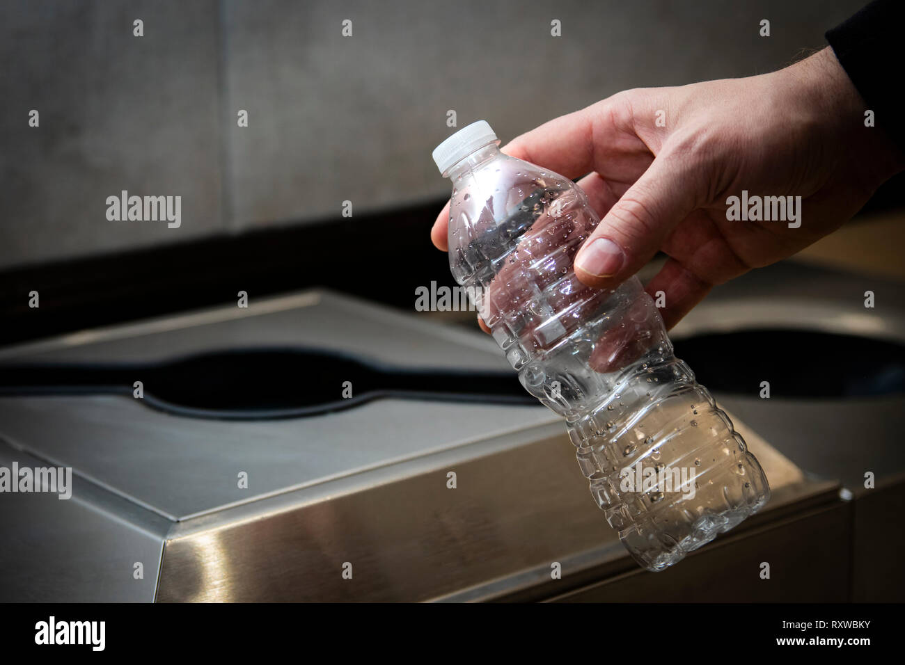 Hand throwing disposable plastic water bottle into trash or recycling bin. Stock Photo