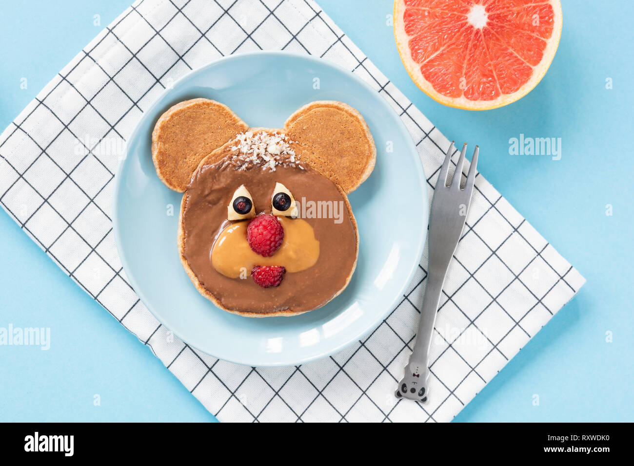 Funny Teddy Bear pancake food art for kids on bright blue background. Top view. Healthy breakfast children meal Stock Photo