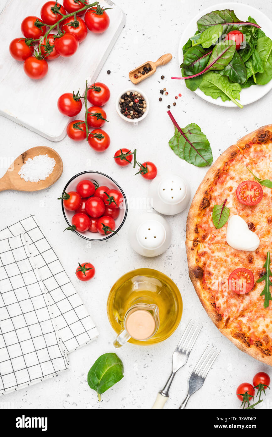 Pizza and italian cuisine food ingredients on white background. Olive oil, tomatoes, seasonings and baked italian pizza. Table top view Stock Photo