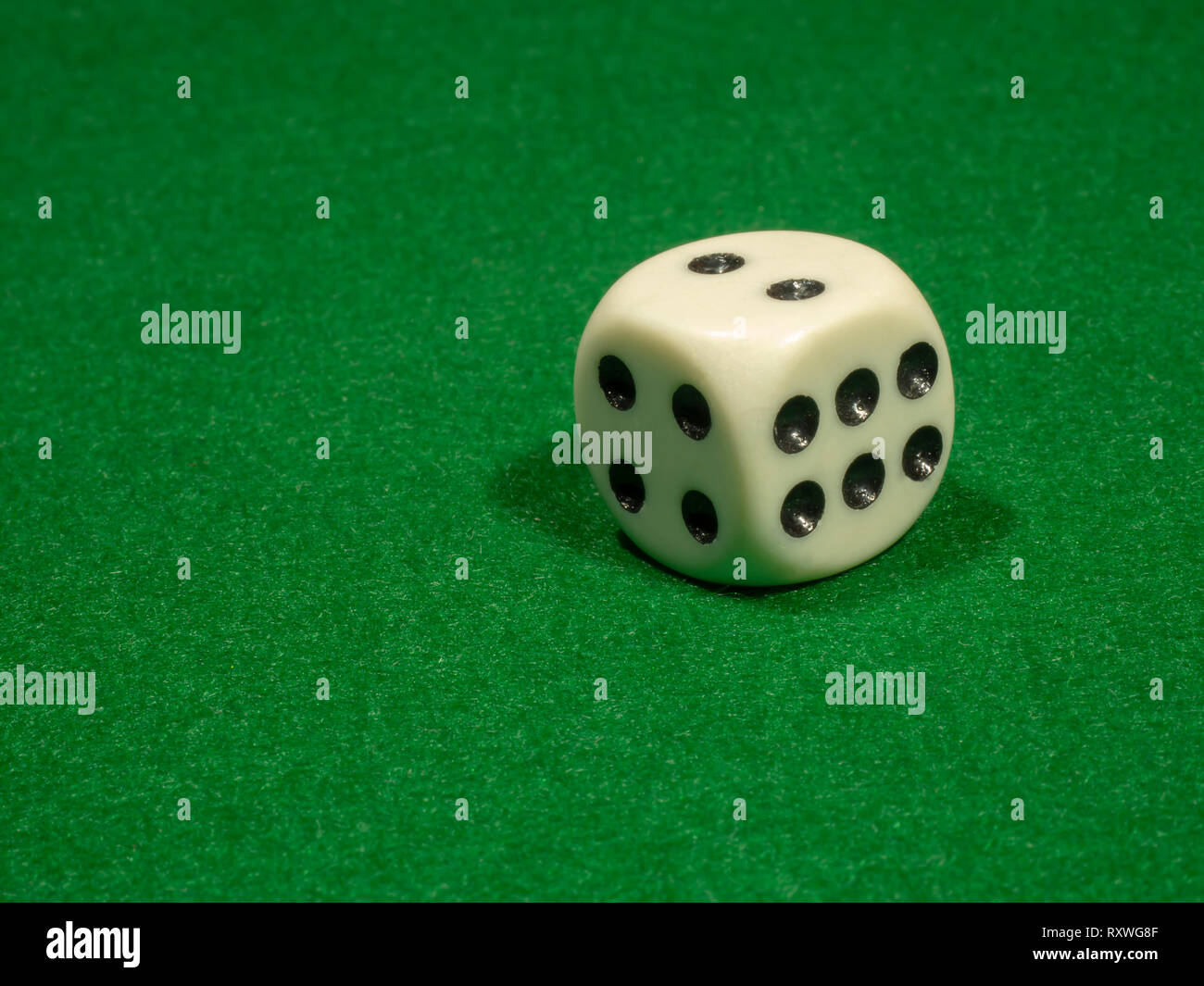 The bone cube of white color with black points for gamblings lies on green cloth. Stock Photo