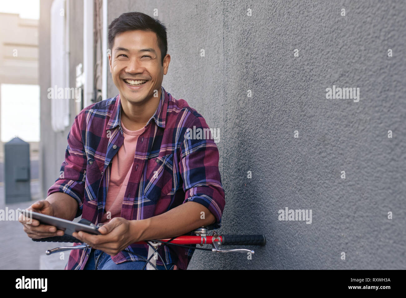 Happy young man leaning on his bicycle using a tablet Stock Photo