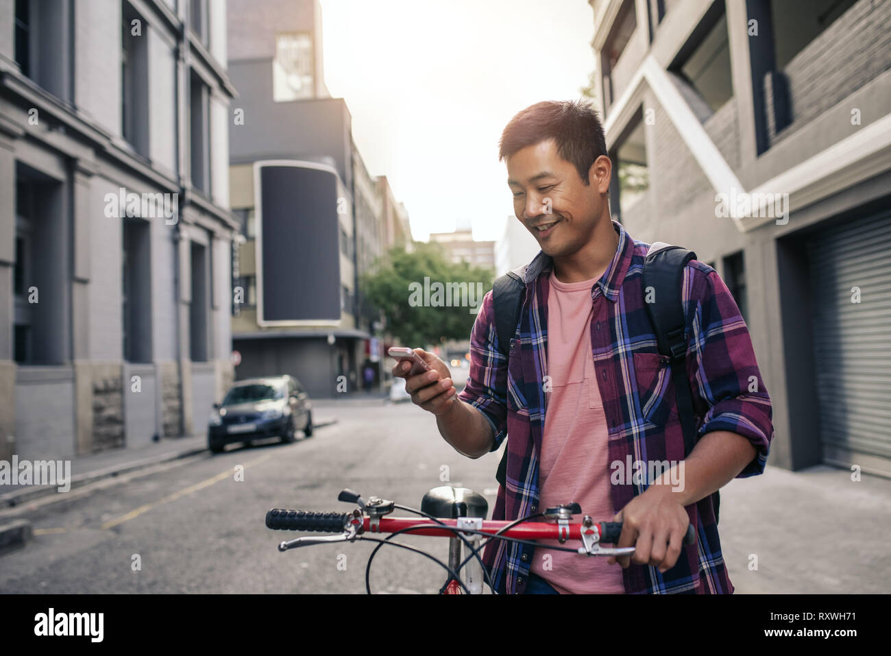 Smiling young man standing with his bike using a cellphone Stock Photo