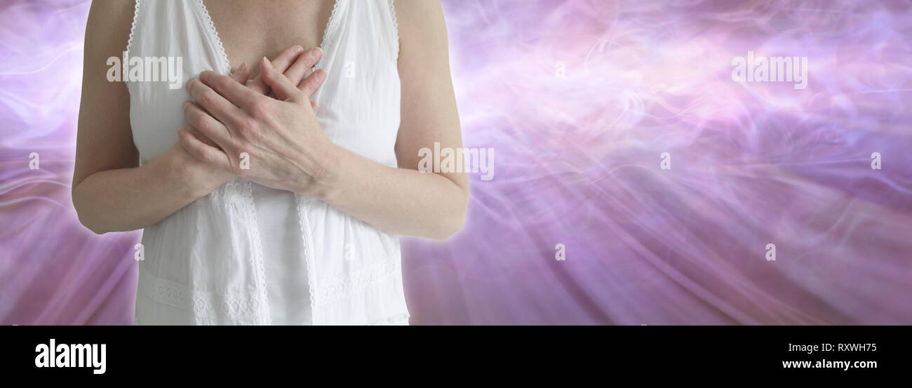 Sending you love from my heart - female in white clothing holding both hands over heart area with an ethereal energy flowing outwards and copy space Stock Photo