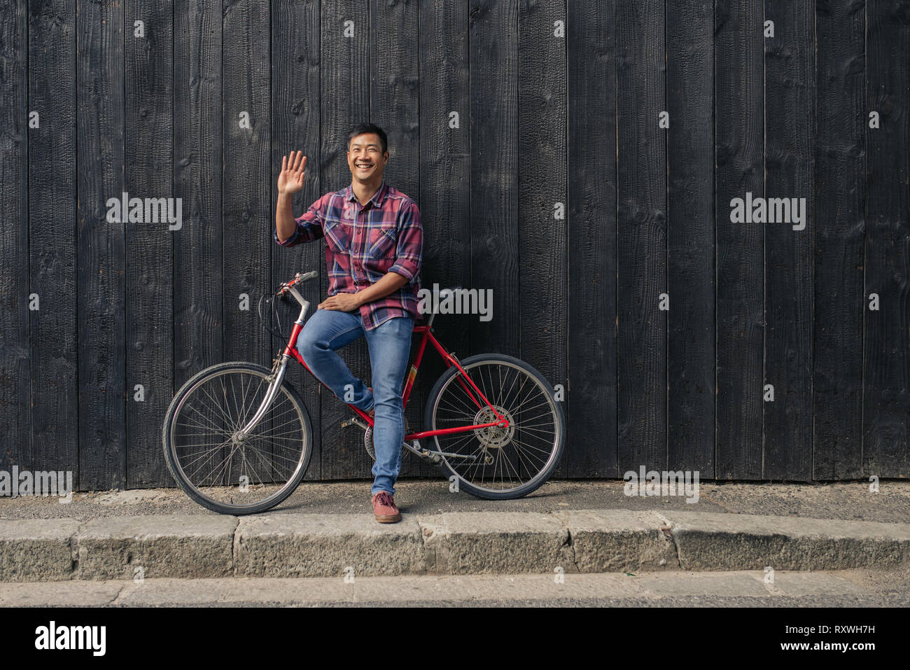 Smiling young man with a bicycle waving hello Stock Photo