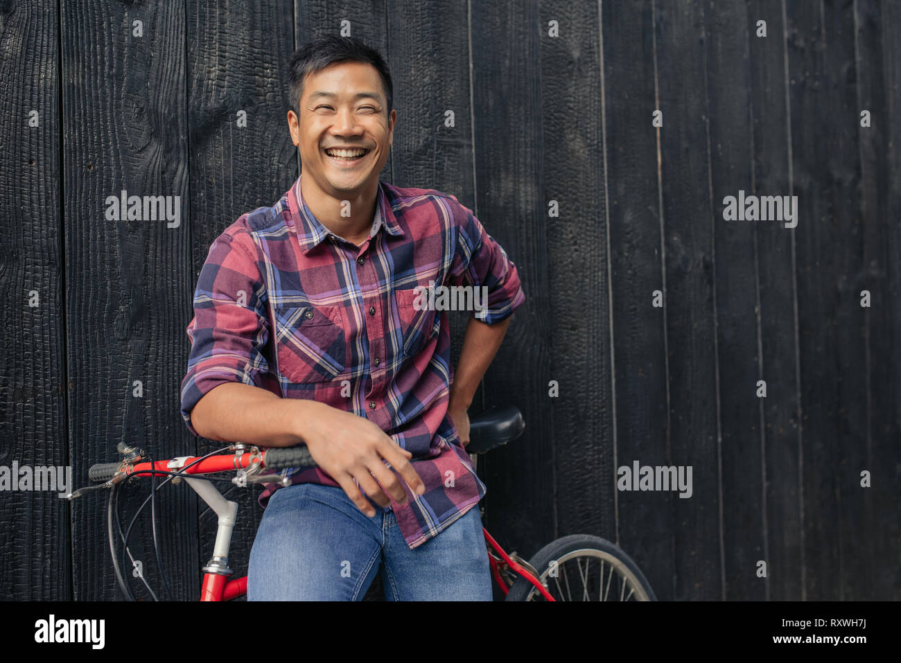 Smiling young man with a bike against a city wall Stock Photo