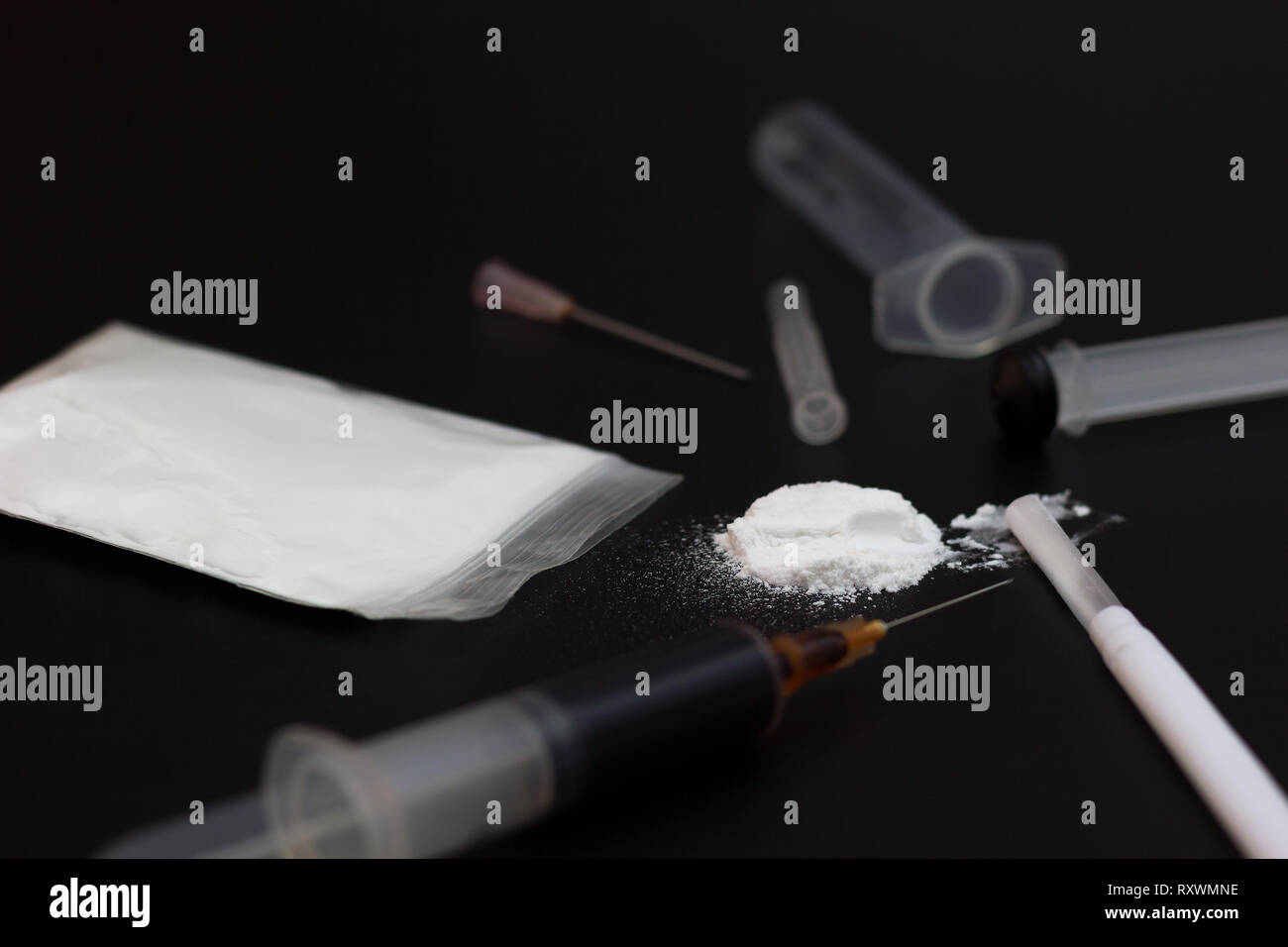 Fake Heroin or diacetylmorphine bag and syringes placed side by side. Low key addictive substance on darkness background. Stock Photo