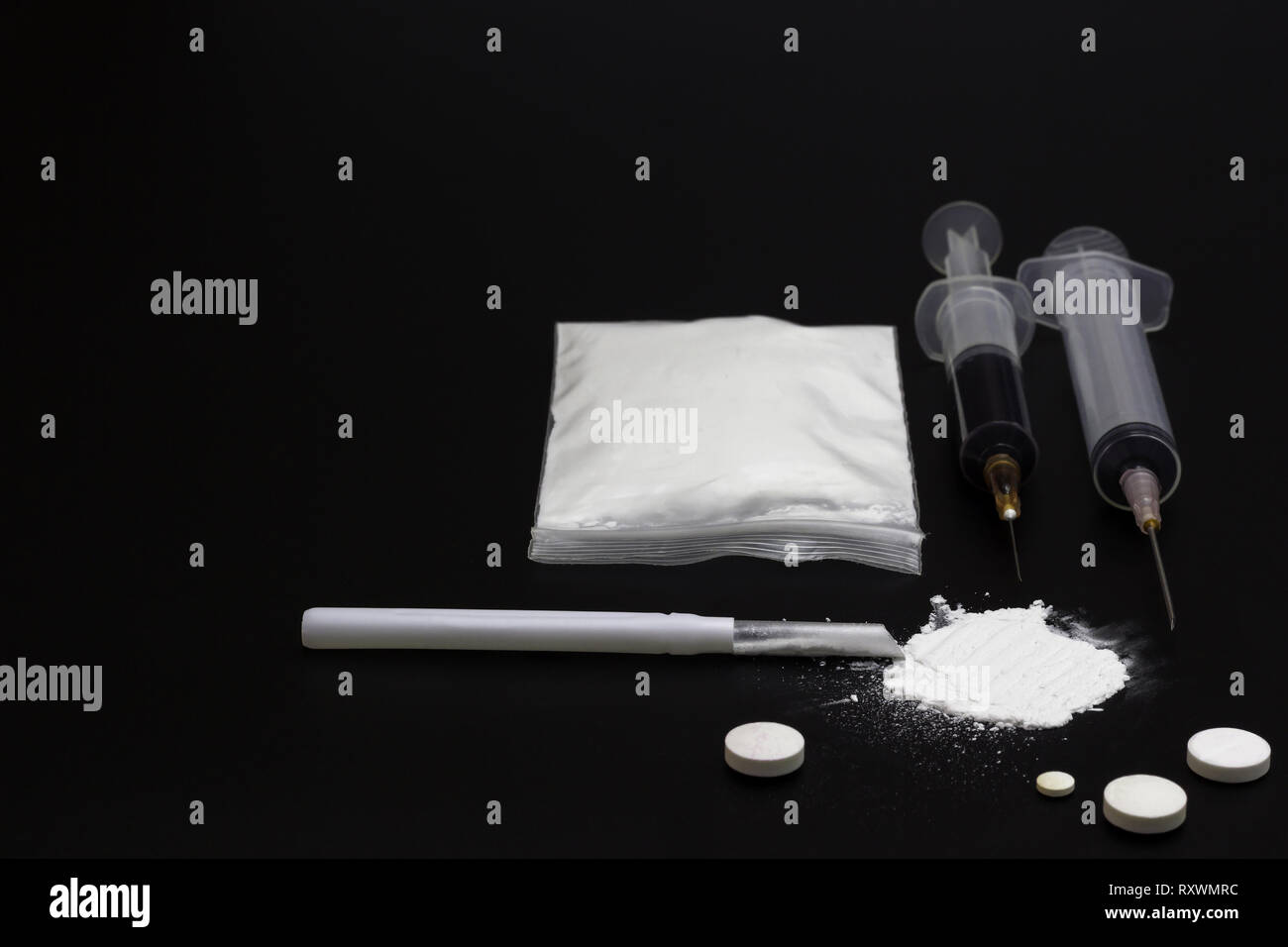 Fake Heroin or diacetylmorphine bag and syringes placed side by side. Low key addictive substance on darkness background. Stock Photo