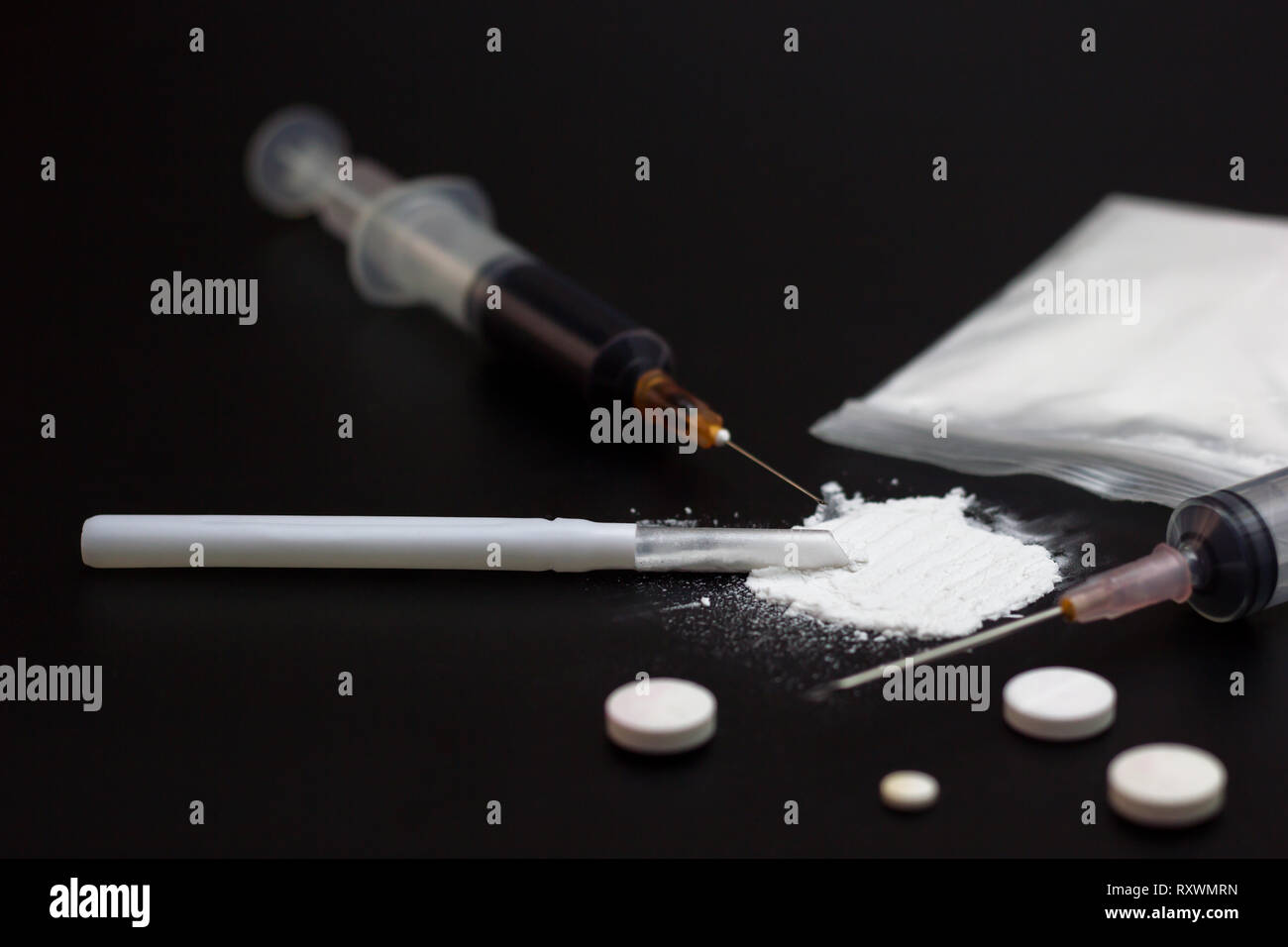 Fake Heroin or diacetylmorphine bag and syringes placed side by side. Low key addictive substance on darkness background. Stock Photo