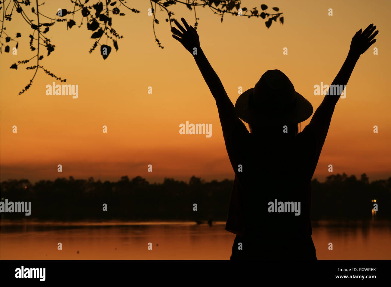 Silhouette of a young woman raising arms against beautiful orange color ...