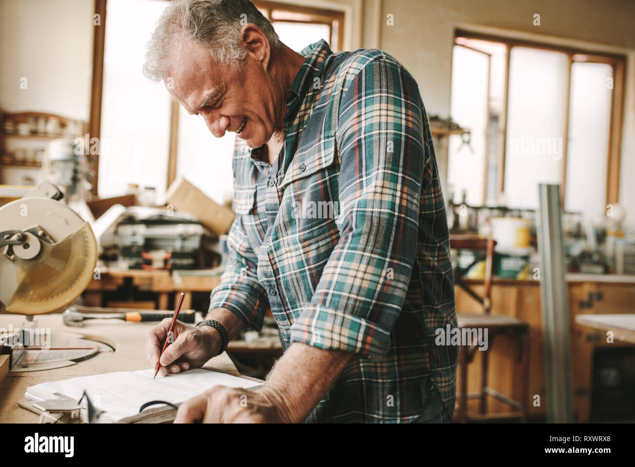Happy senior carpenter preparing drawing for furniture parts. Man making designs on paper with