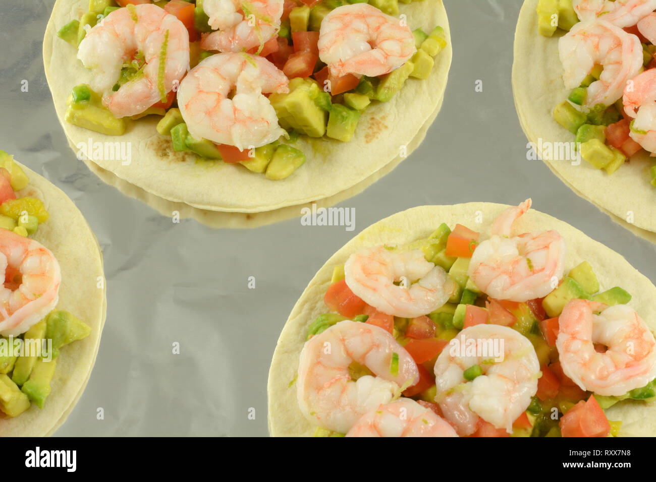 Shrimp tostados with chopped avocado and tomatoes on aluminum foil