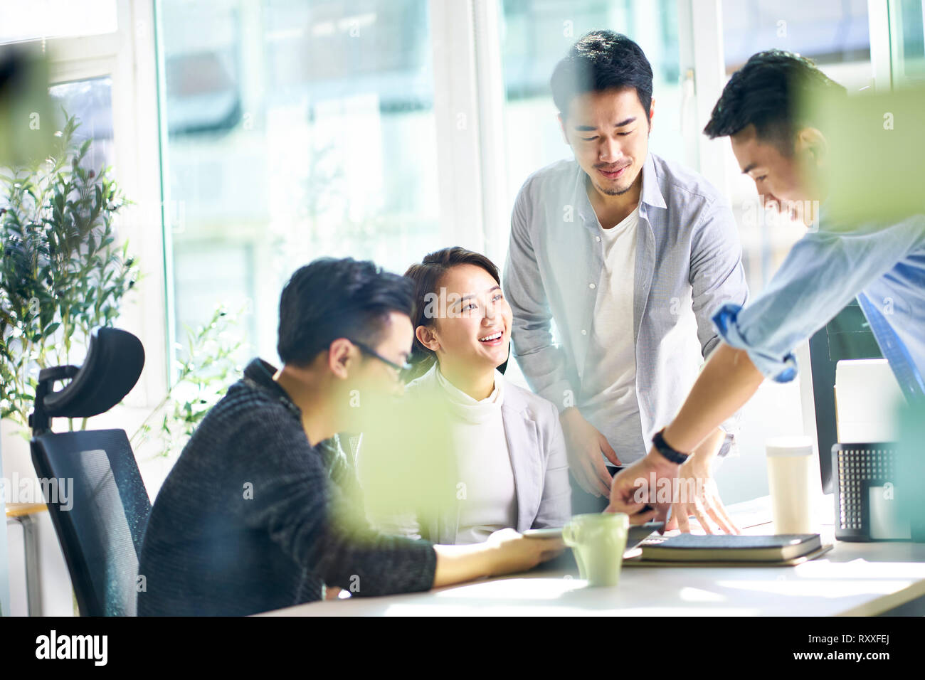 group of four happy young asian corporate executives working together meeting in office discussing business in office. Stock Photo