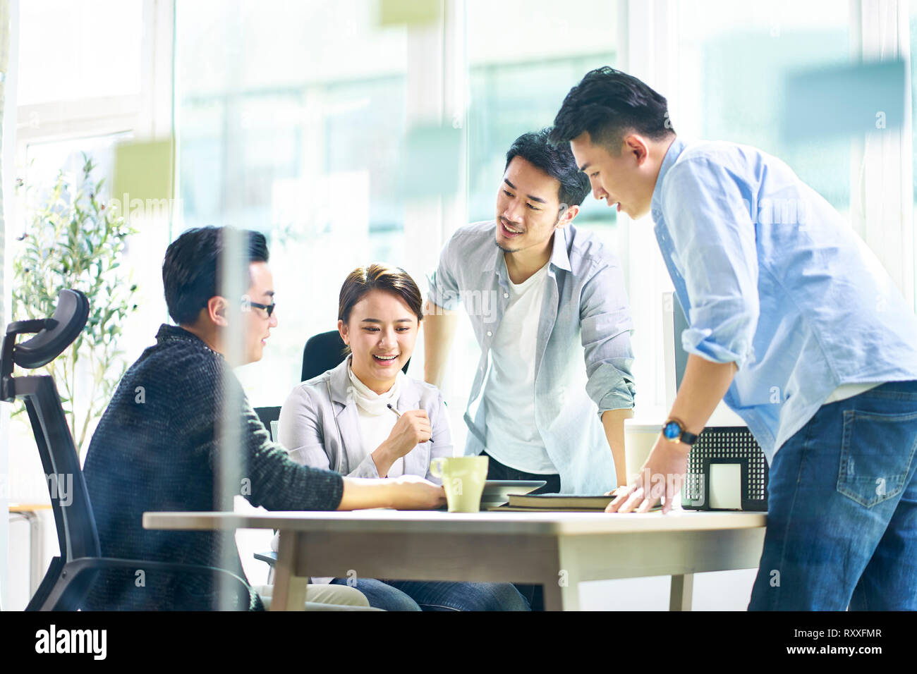 group of four happy young asian corporate executives working together meeting in office discussing business in office. Stock Photo