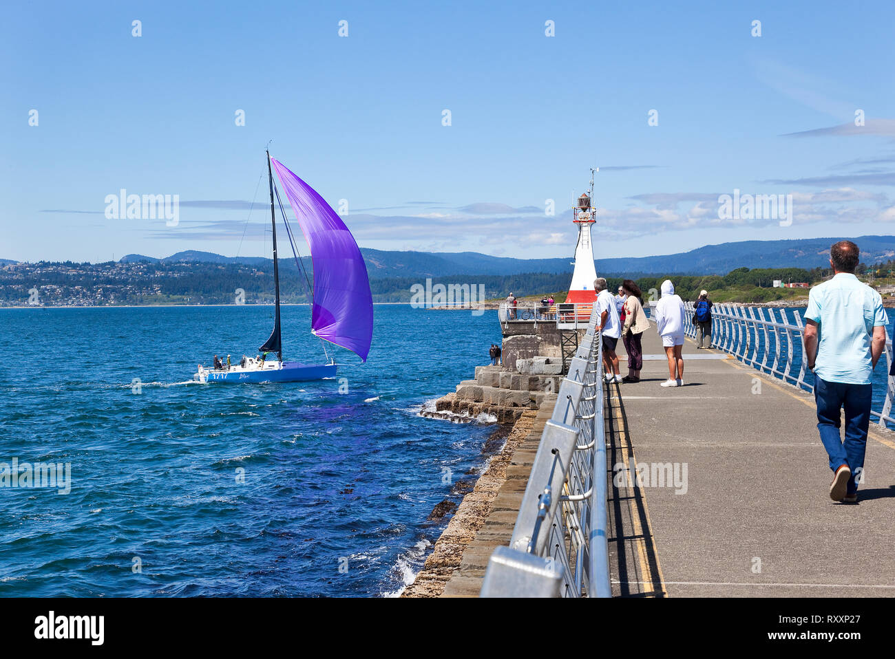 Sail boat passing close by the Ogden Point Breakwater Lightouse toward the calm waters of the Victoria Harbour. Victoria, British Columbia, Canada Stock Photo