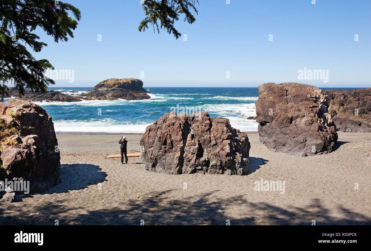 Man taking a photo while surrounded by massive rock formations on a beach at the end of the South Beach Trail, Pacific Rim National Park, Vancouver Island, British Columbia, Canada Stock Photo