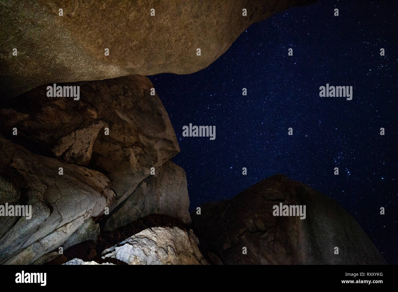 A luminescent pearly moon crosses over the crevice of a desert boulder. Stock Photo