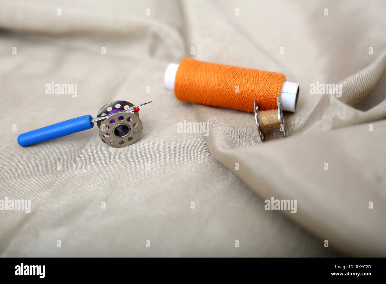 Picture of orange sewing thread, needle ripper and two bobbin on the