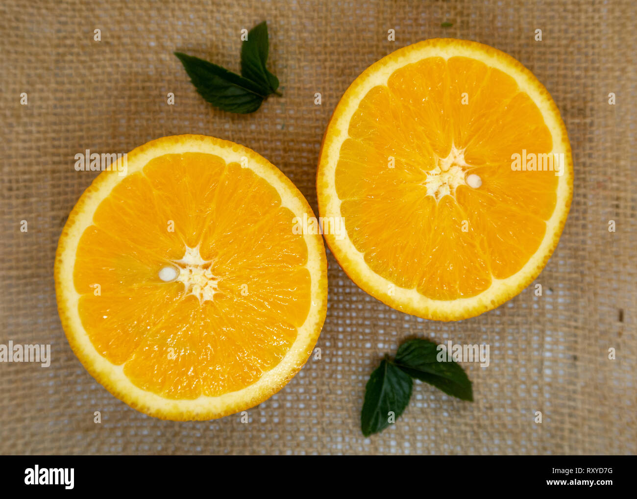 Cut fresh juicy orange halves on a hessian background Stock Photo