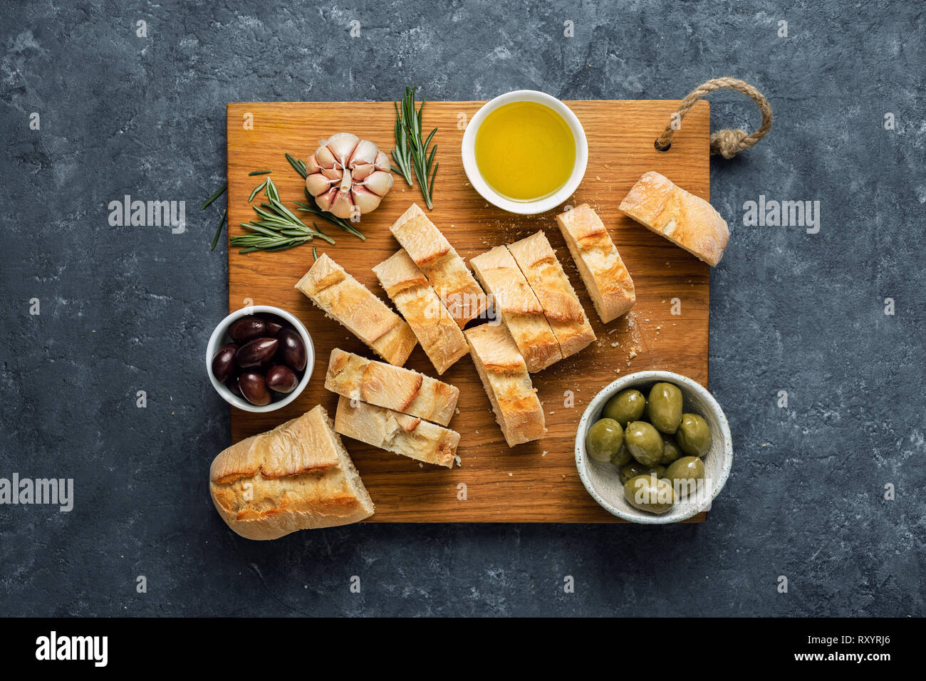 Italian food concept. Cooking Italian bruschetta. Olives, fresh baguette slices, olive oil, garlic and rosemary on dark stone background top view Stock Photo