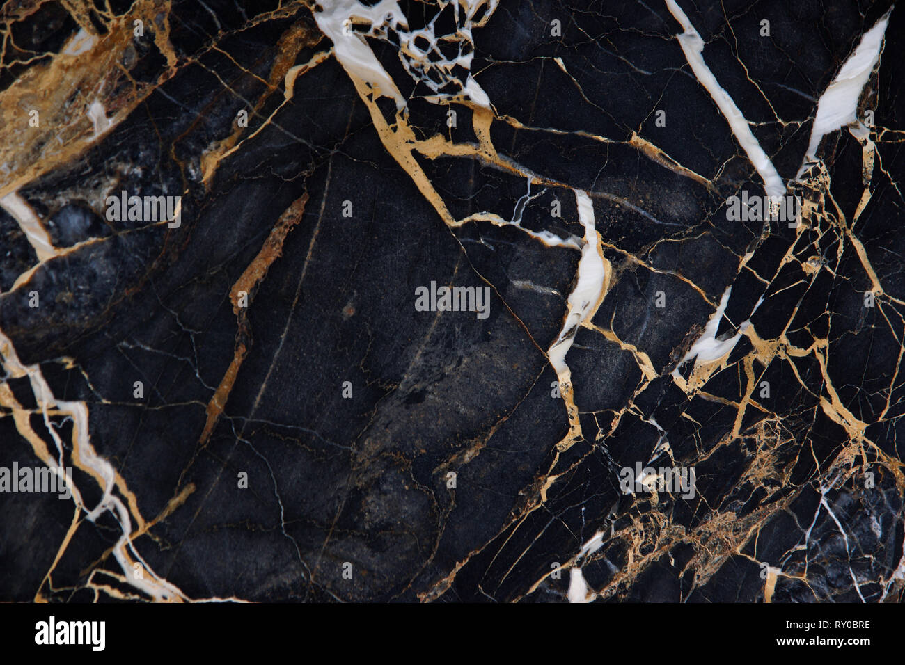 The surface of a slab of black marble with yellow and white veins is