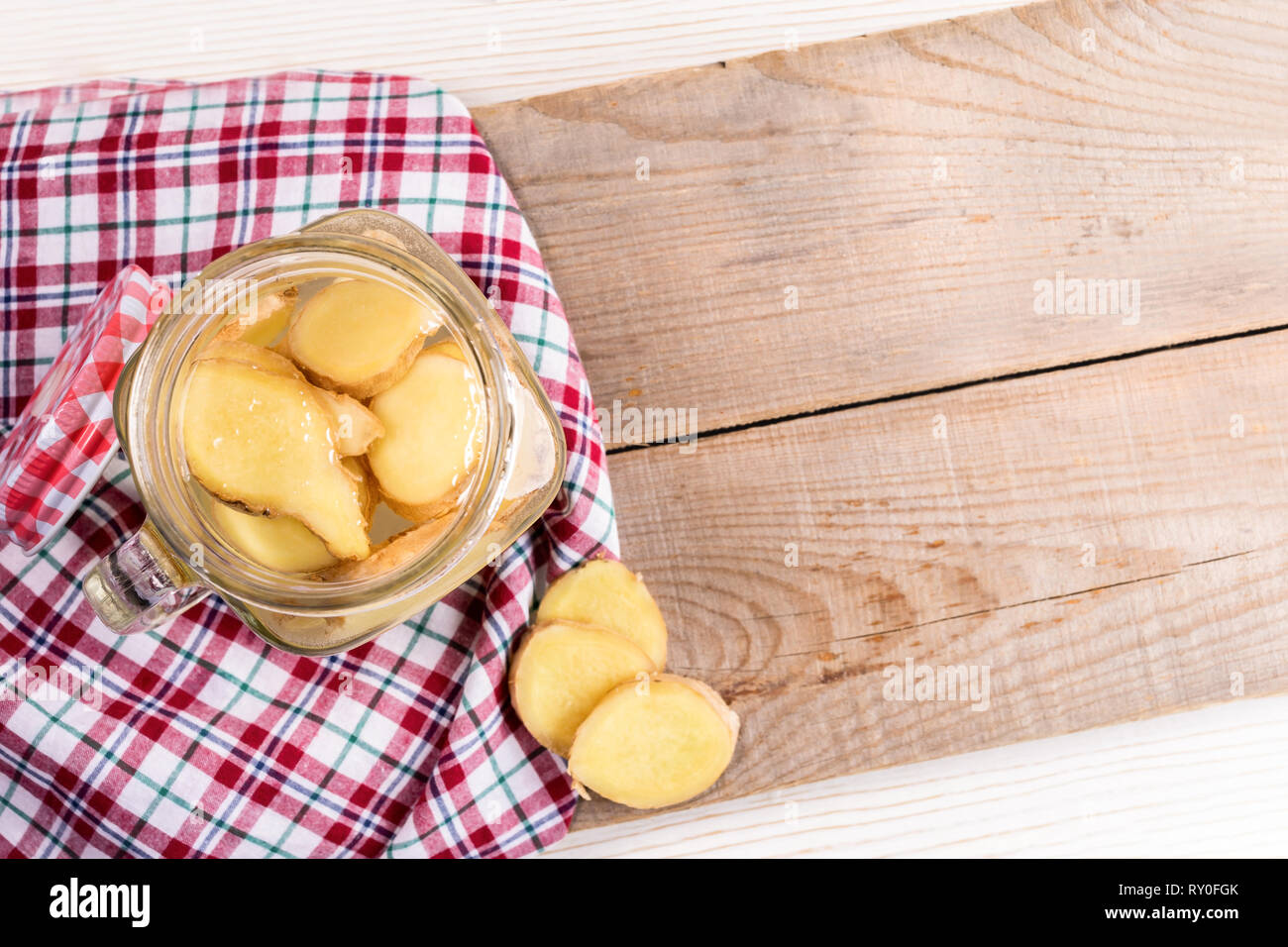 Opened glass jar with ginger water on red tartan cloth on diagonal wooden boards.  Stock Photo