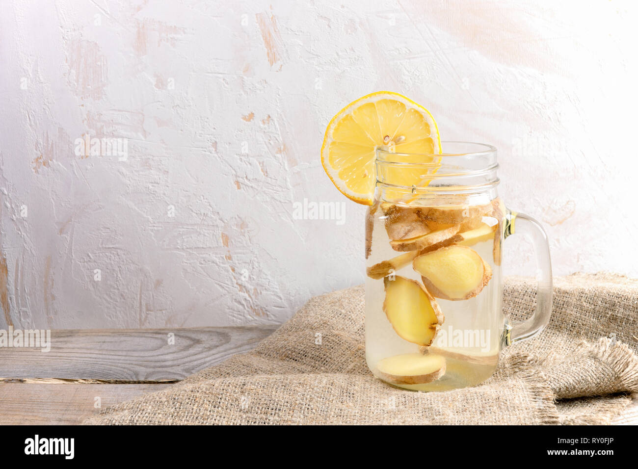 Glass jar with ginger water on burlap on wooden table on light  background.  Stock Photo