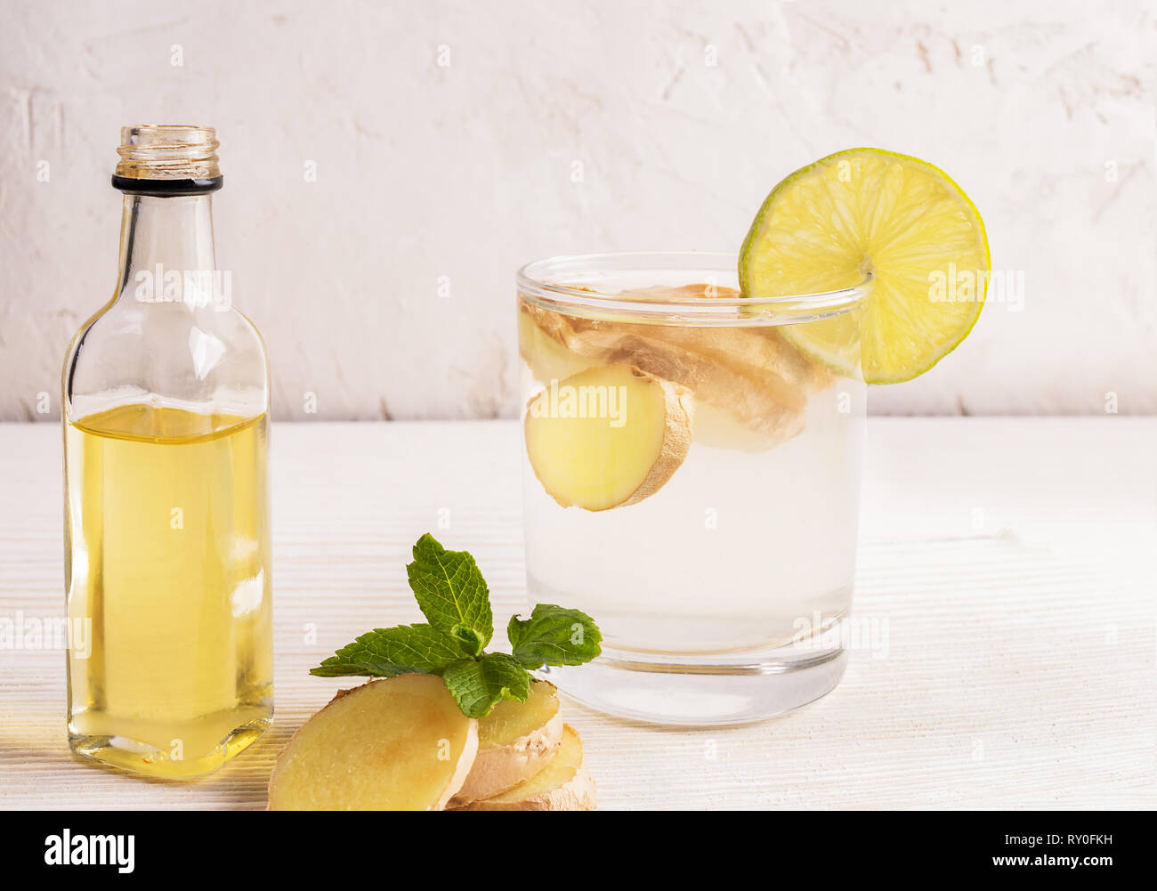 Glass with ginger water and bottle of ginger oil on white table on light  background.  Stock Photo