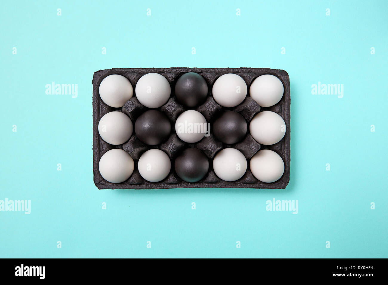 Pattern of white and painted black eggs in a black cardboard box on a blue background with copy space. Easter composition. Flat lay Stock Photo