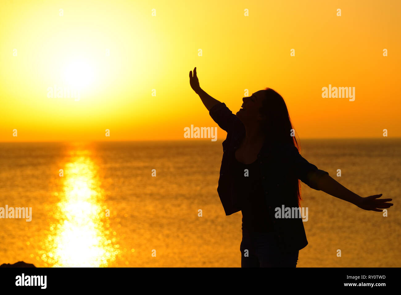 Silhouette of an excirted girl stretching arms at sunset celebrating success on the beach Stock Photo