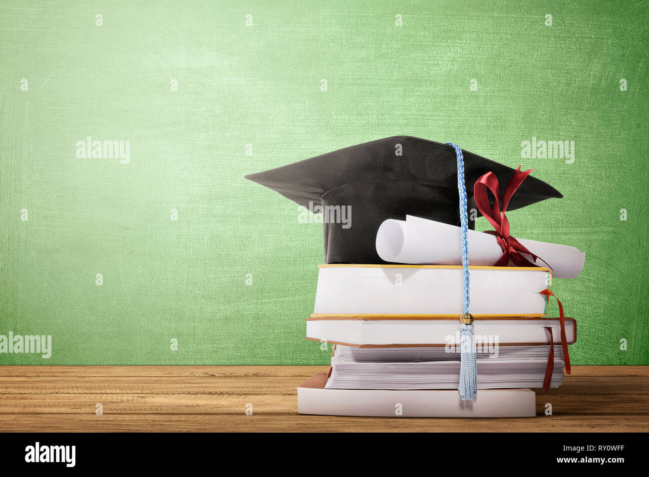 Graduation hat, diploma scroll and books on the wooden table with ...