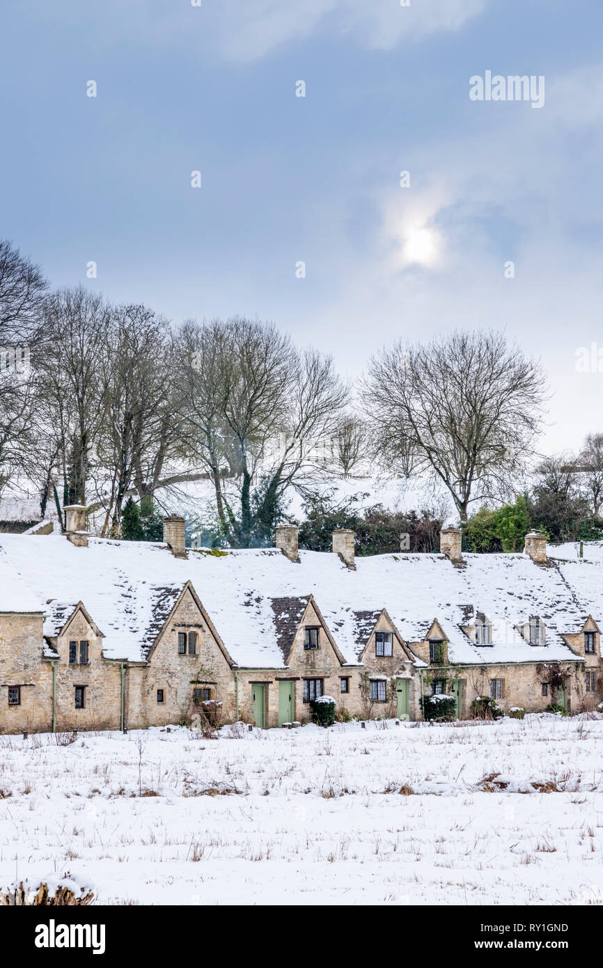 Arlington Row covered with snow under a pale wintry sky at Bibury, Gloucestershire UK Stock Photo