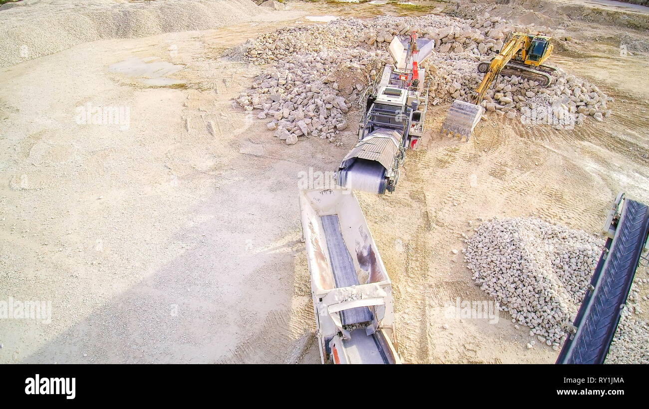 The big trucks and machineries in the quarry area. There are limestone crusher and the backhoe surrounded with big stones Stock Photo