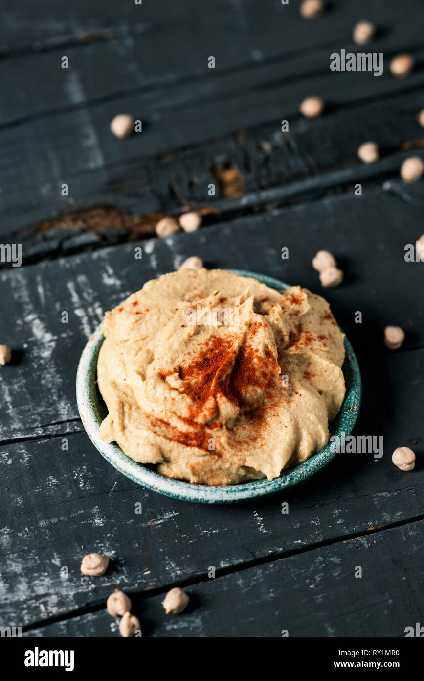 high angle view of a green ceramic plate with homemade hummus seasoned with paprika, on a dark gray rustic wooden table Stock Photo