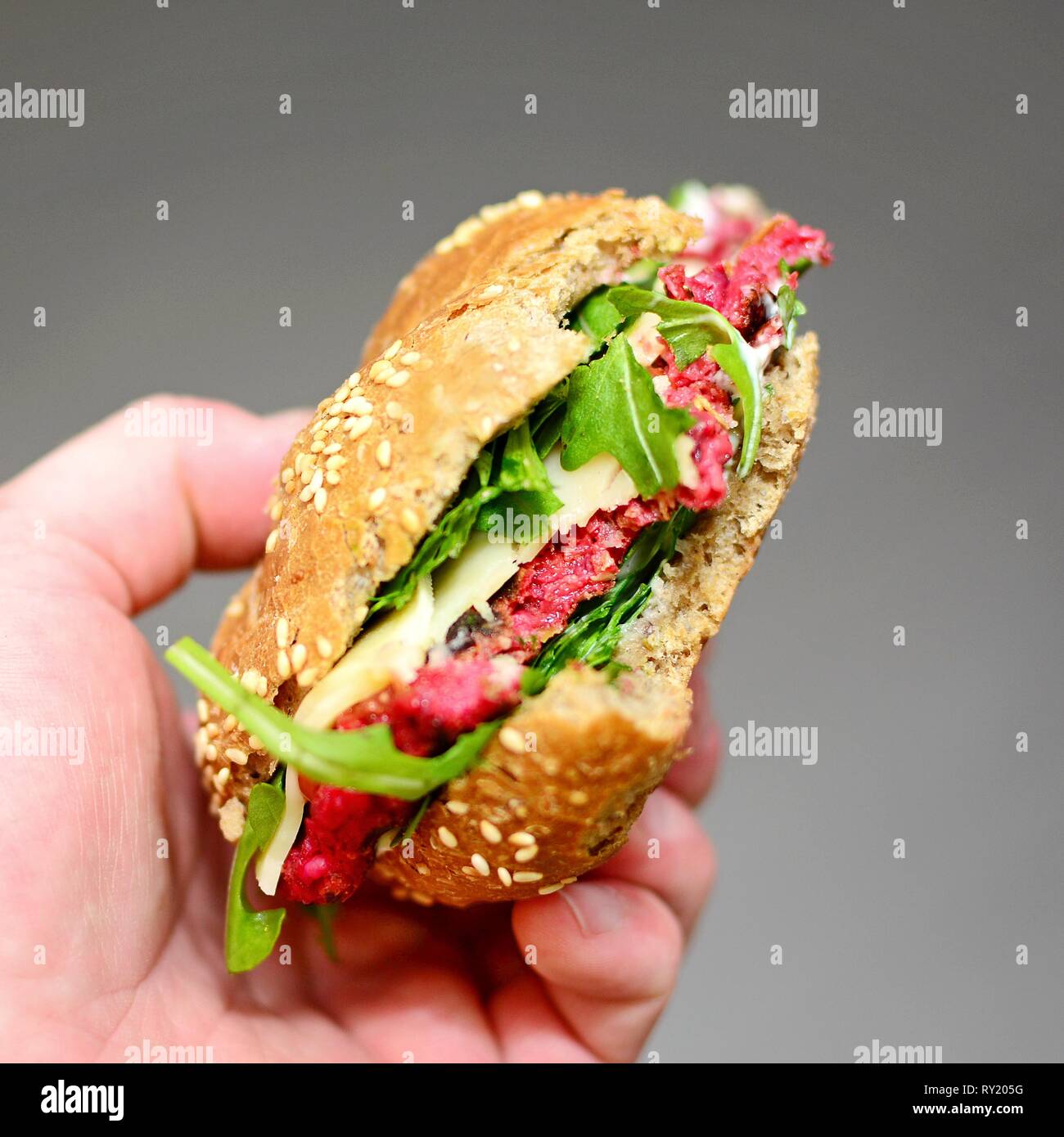 Mans Hand Holding a Beetroot and Arugula Burger with Missing Bites. Stock Photo
