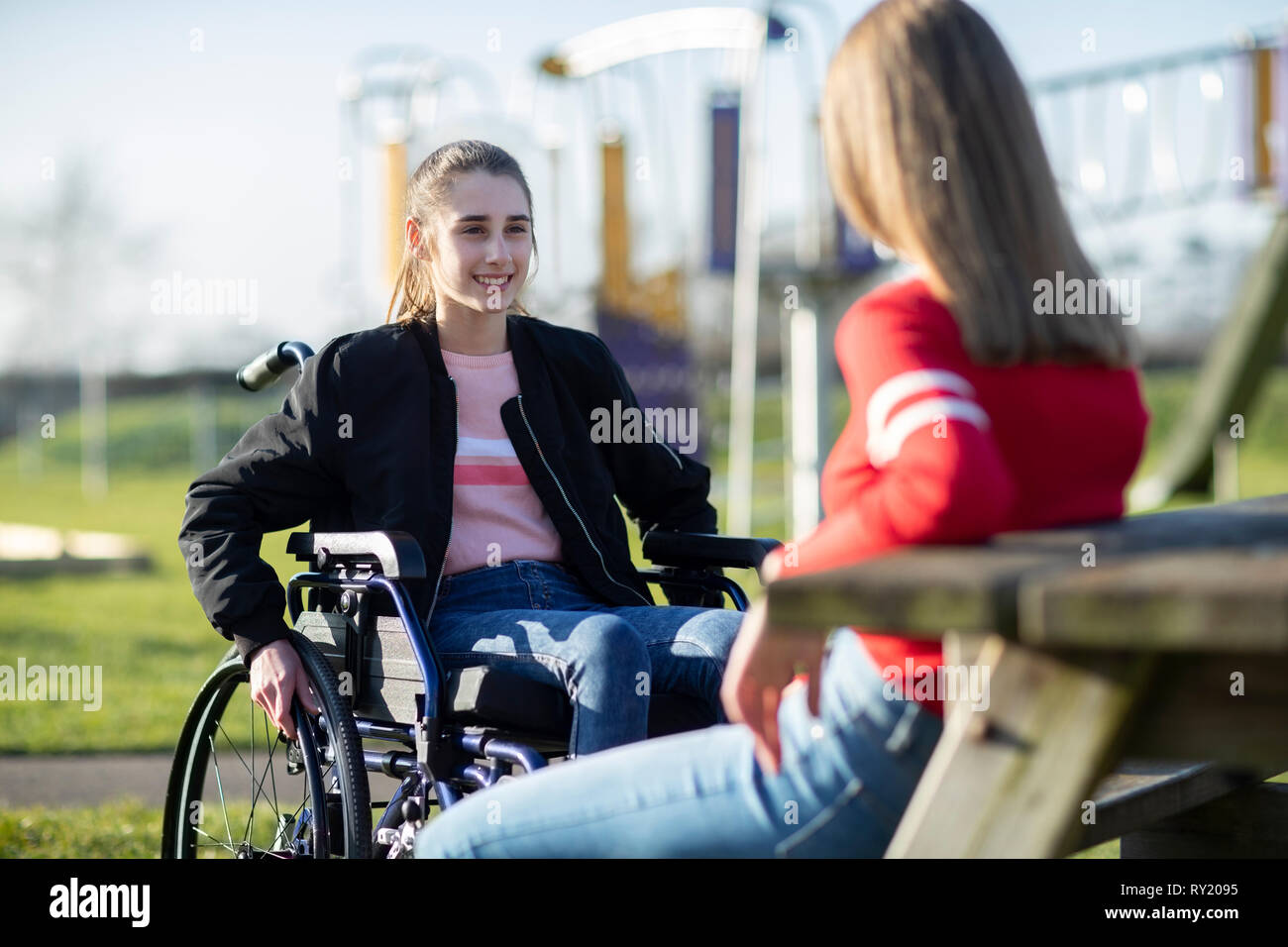 Teenage Girl In Wheelchair Talking With Friend In Park Stock Photo