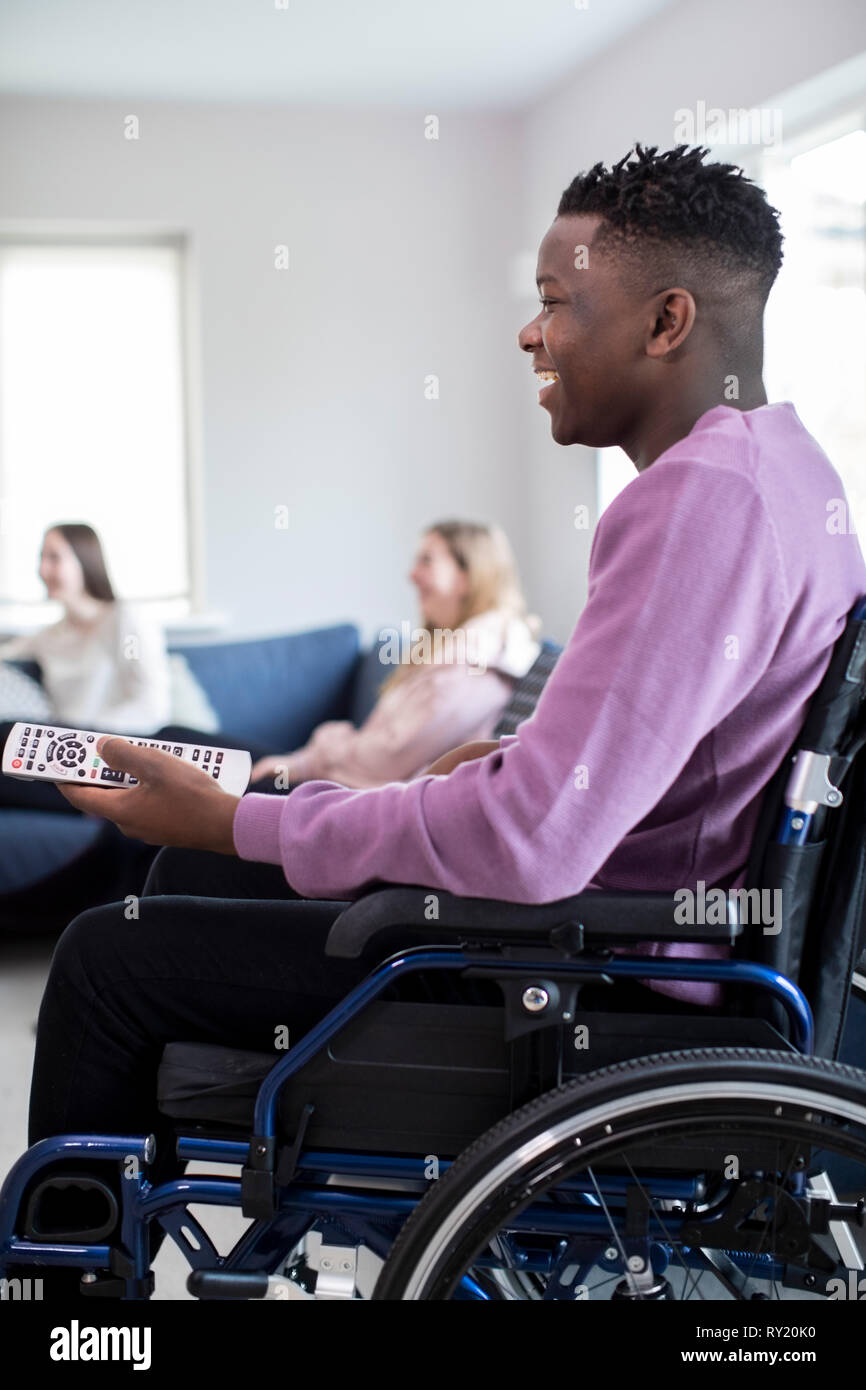 Teenage Boy In Wheelchair Watching Television With Freinds At Home Stock Photo