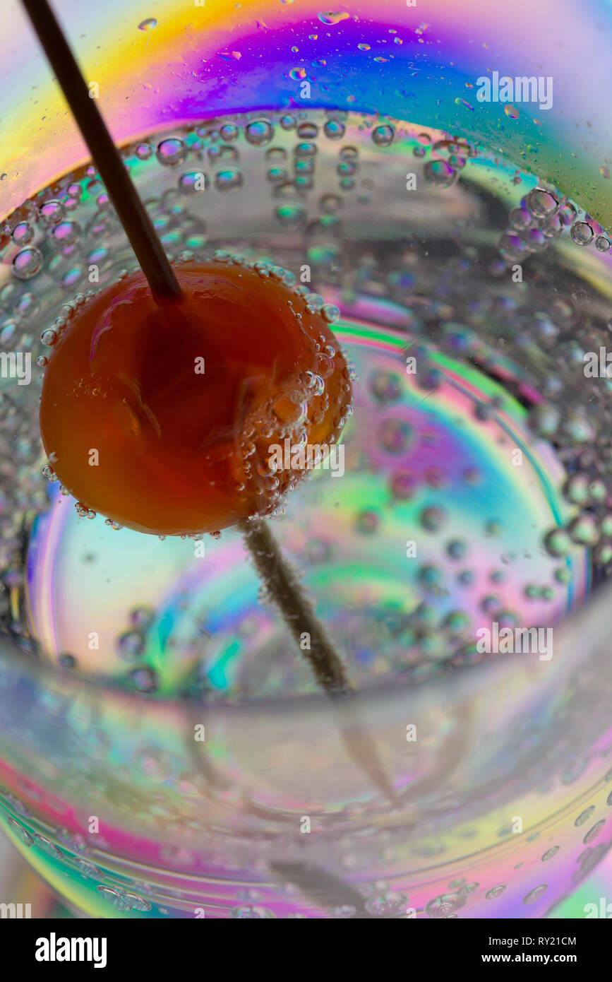 Interesting stress patterns in plastic wine glass seen with red cherry on cocktail stick in gin and tonic drink giving weird appearance Stock Photo