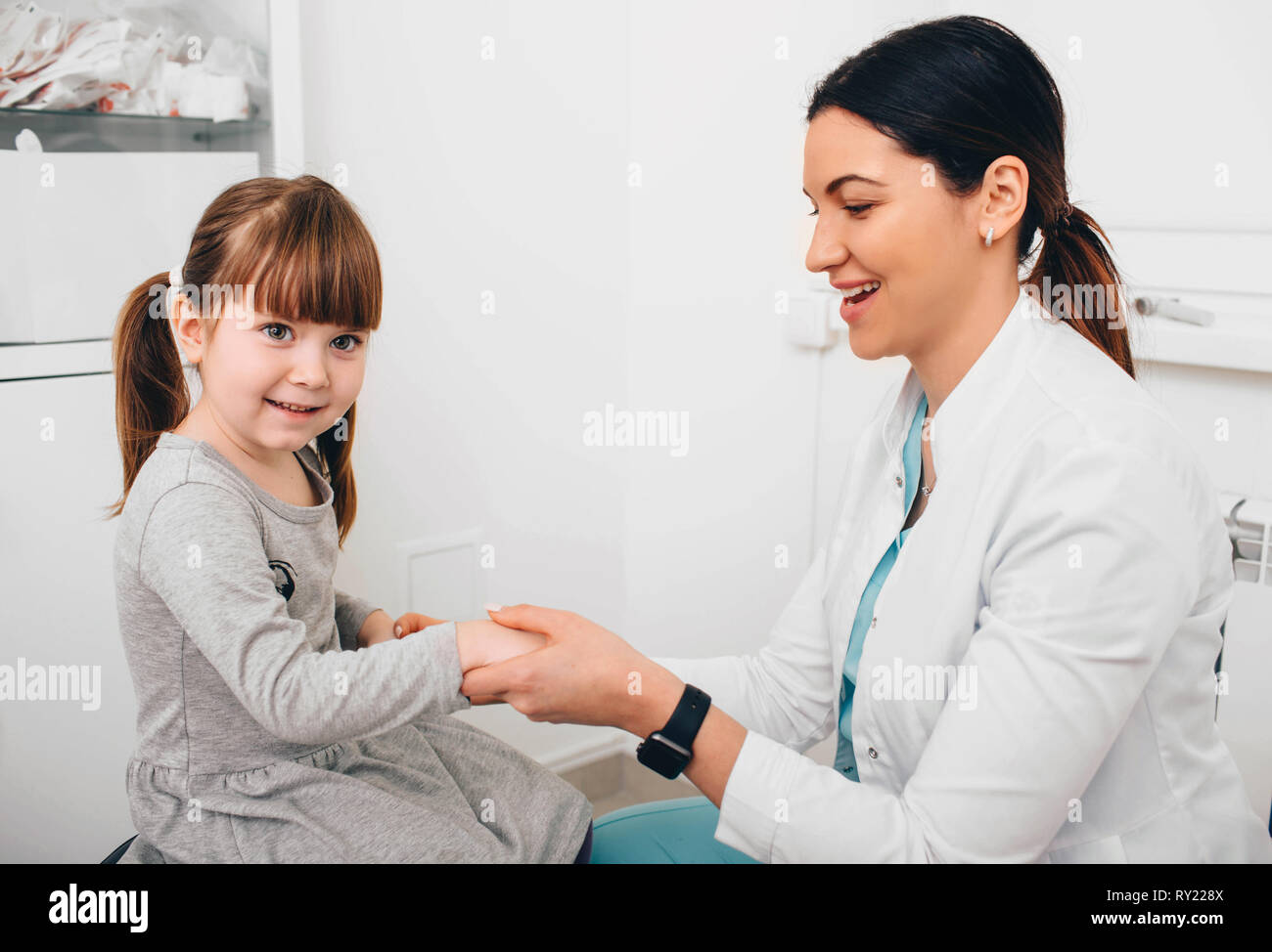 Cheerful pediatrician greets a little patient's. Doctor holding child's hand in comfort Stock Photo