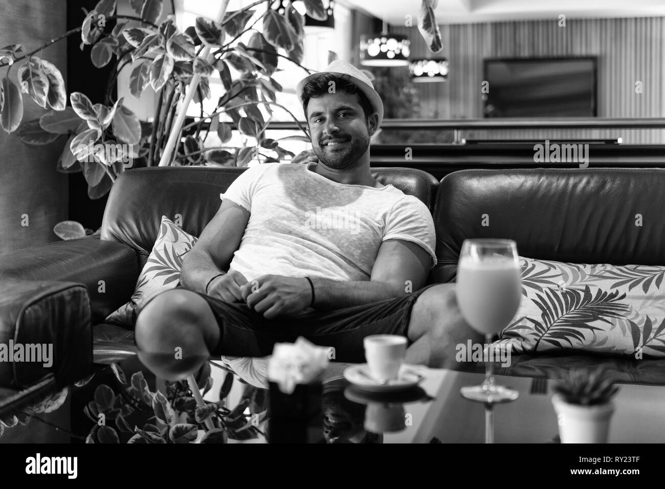 Happy Young Man Sitting Relaxed on Sofa at Luxury Hotel Lobby Bar Stock Photo
