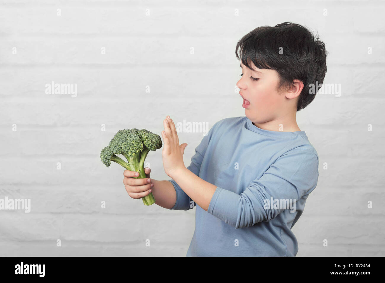 Child do not like to broccoli against brick background Stock Photo