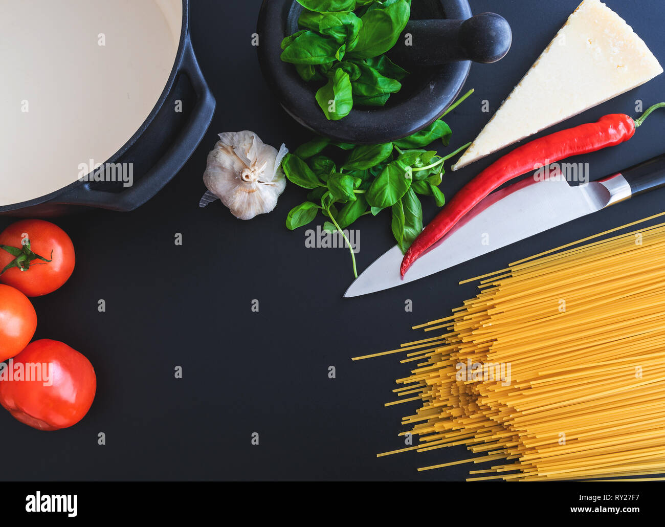 preparing italian pasta with fresh basil in mortar, tomatoes, garlic, pepper and Parmesan cheese on dark kitchen counter Stock Photo