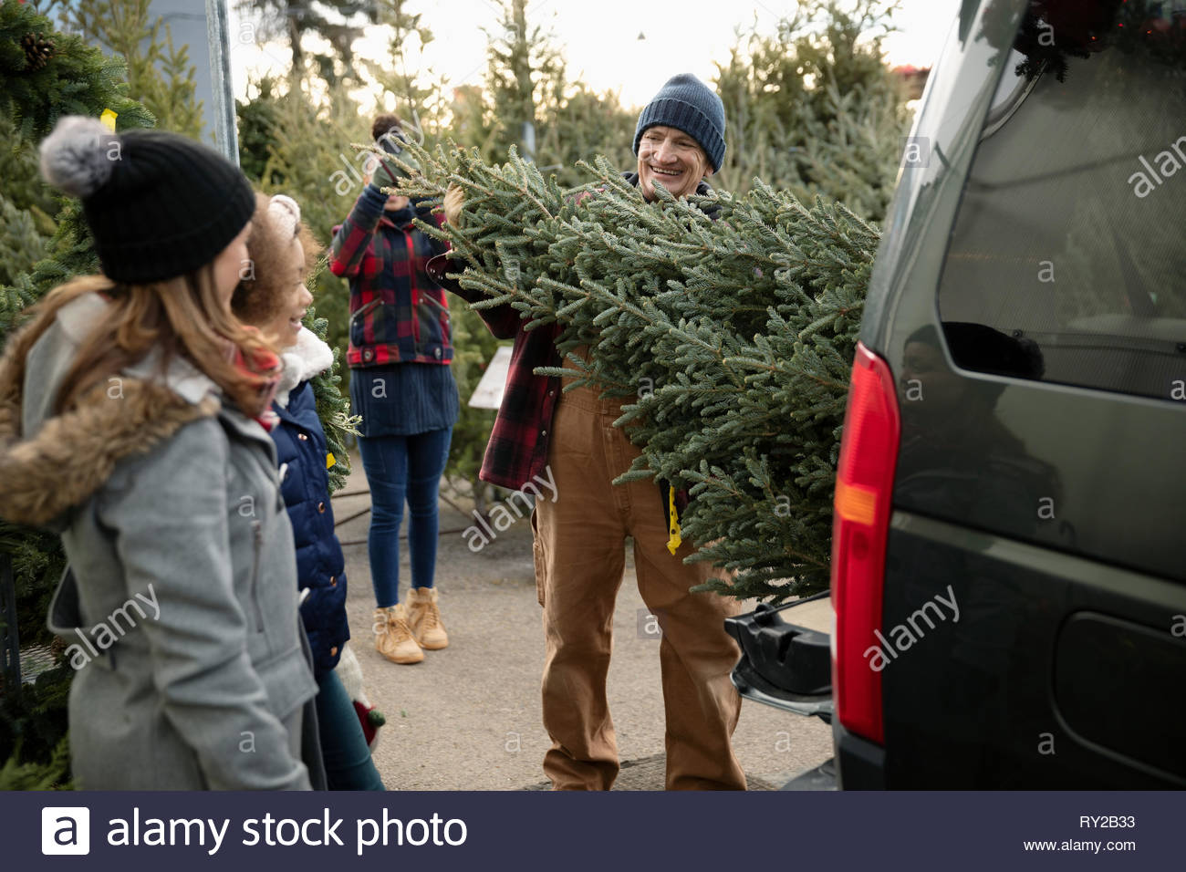 Worker helping family load christmas tree into SUV at christmas market