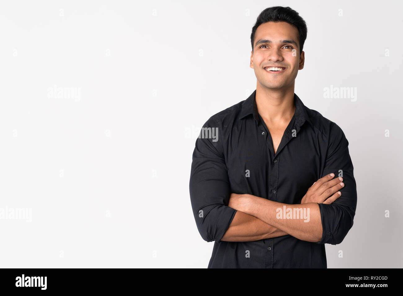 Portrait of young happy Indian businessman thinking with arms crossed ...
