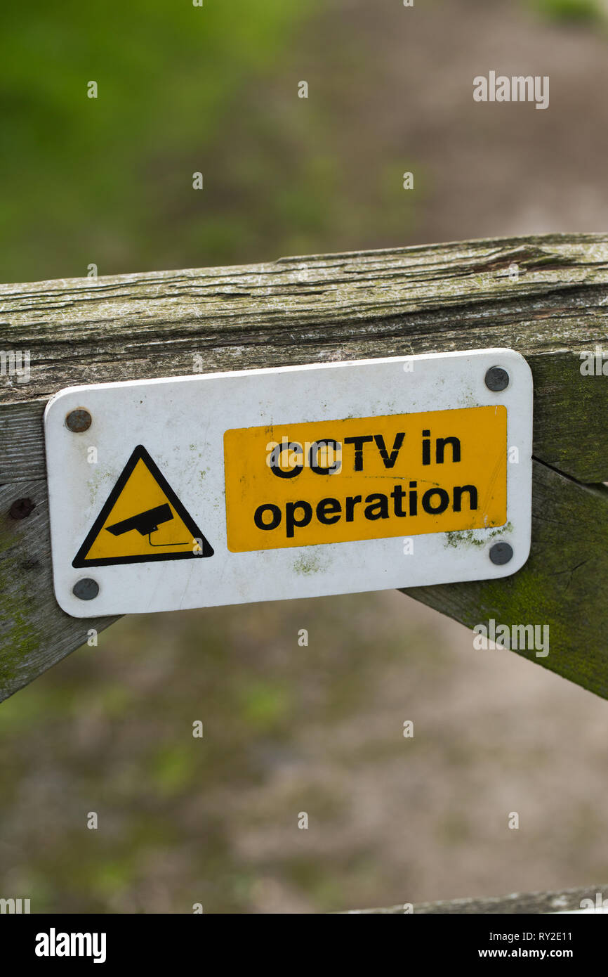 Warning sign on a wooden, timber, farm field gate. CCTV in operation. On a locked farm gate. Registering an owner's fear of domestic livestock theft. Stock Photo