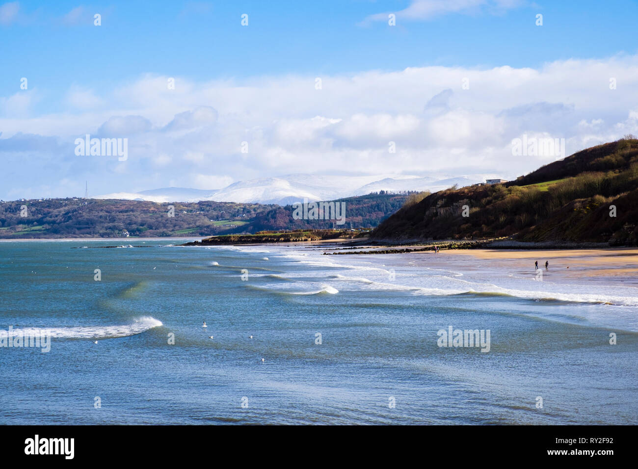 View across Benllech Bay and beach in sunshine with snow on distant mountains of Snowdonia. Benllech, Isle of Anglesey, North Wales, UK, Britain Stock Photo