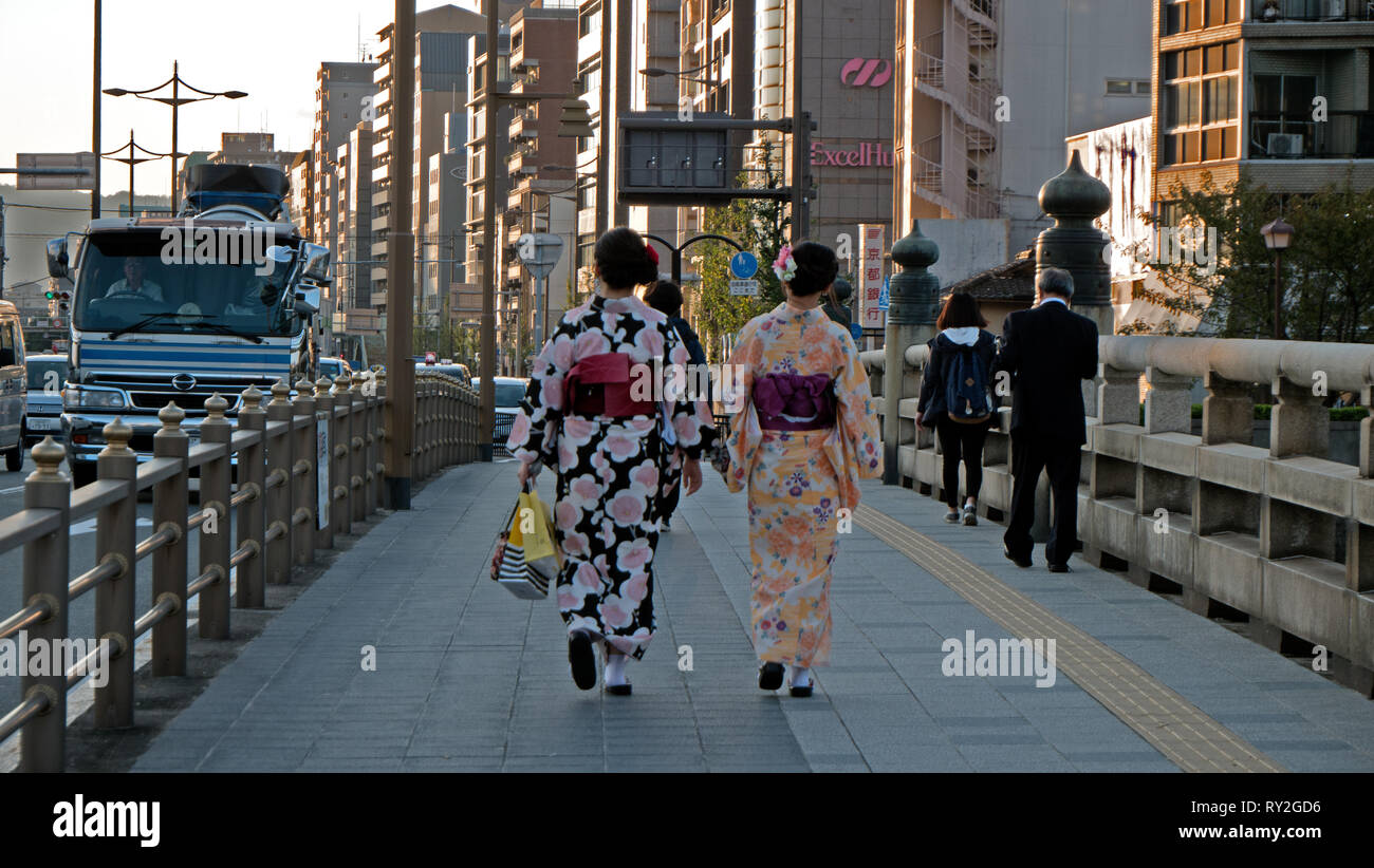 2 Geisha girls walk down a busy street dressed in their traditional dress in Kyoto, Japan. Stock Photo