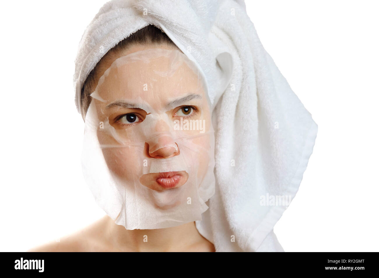 close-up portrait angry beautiful model with facial mask on white background, puffed out her cheeks, angry white towel on head Stock Photo