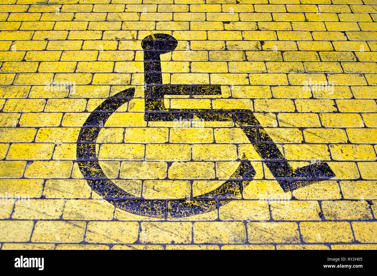 Wheelchair icon in black on yellow pavement indicating a parking place for disabled visitors Stock Photo